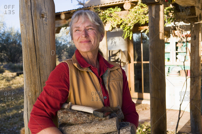 Mature woman at home on her property in a rural setting carrying logs