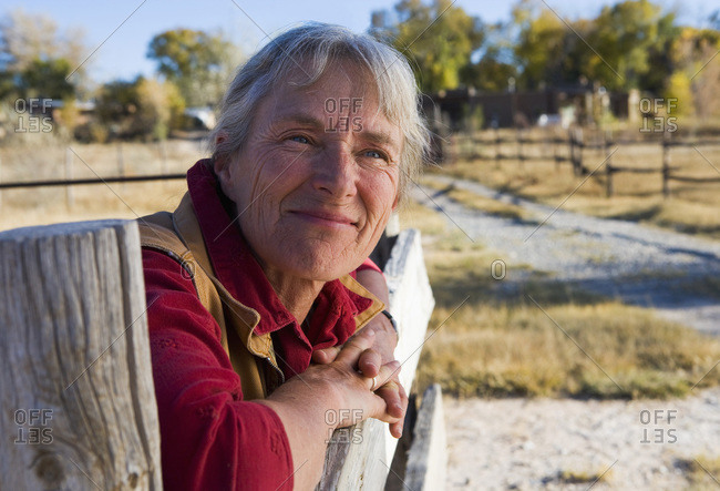 Mature woman at home on her property leaning on a gate.