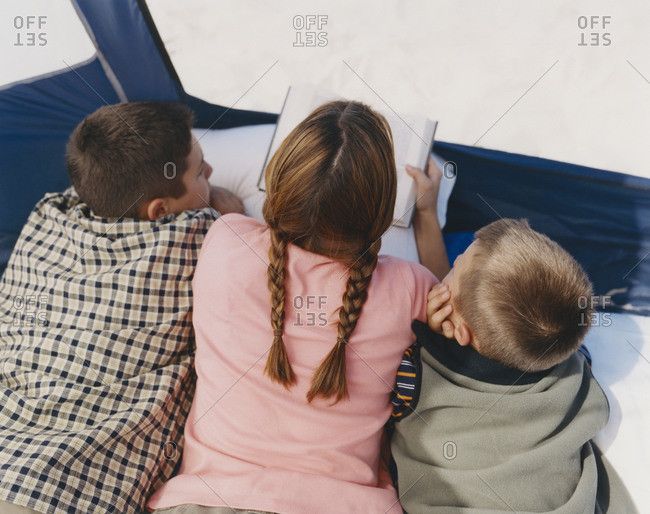Mother reading to her two sons in camping tent