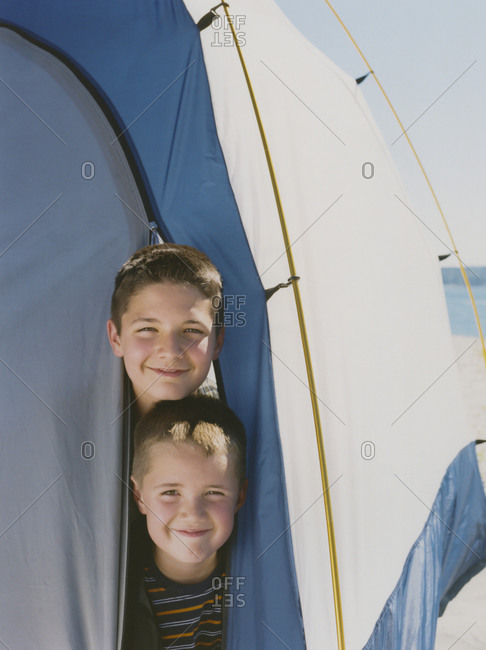 Two young brothers peeking out from inside camping tent