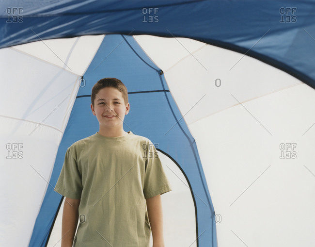 Happy adolescent boy standing upright in a dome camping tent