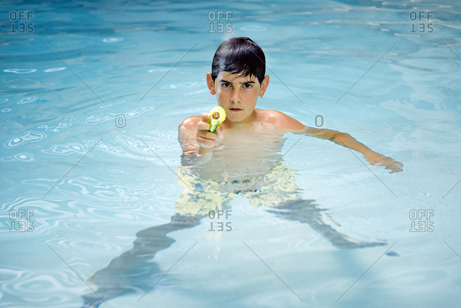 Handsome, dark-haired boy playing with a water gun in the pool water