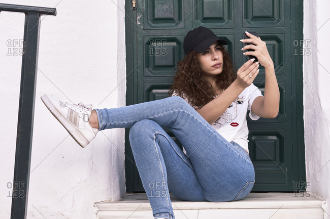 Young woman uses her phone sitting in front of a wooden door