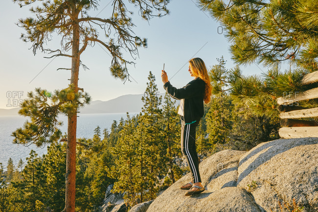 Young woman taking a picture of sunset over Lake Tahoe.