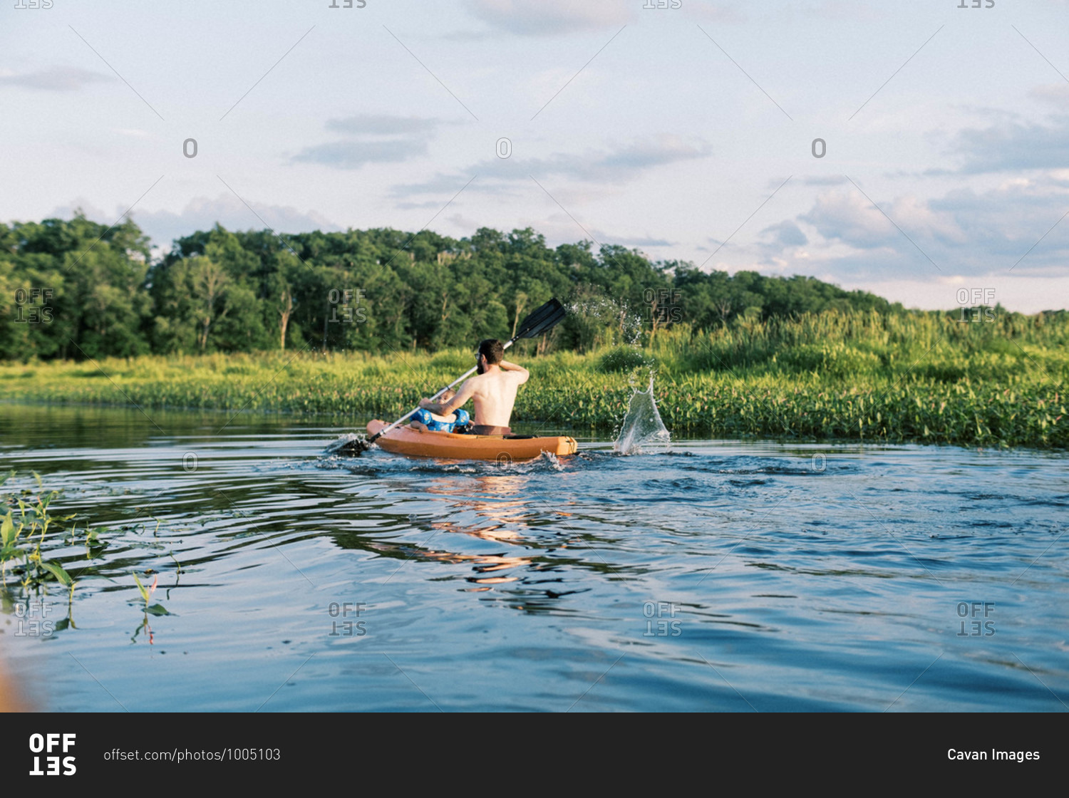 A father and son traveling a river together in their kayak at sunset