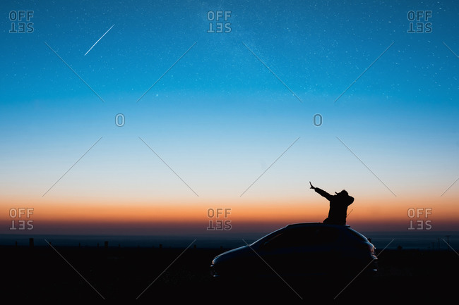 Young man sitting on car doing a Dub in the blue hour of sunrise