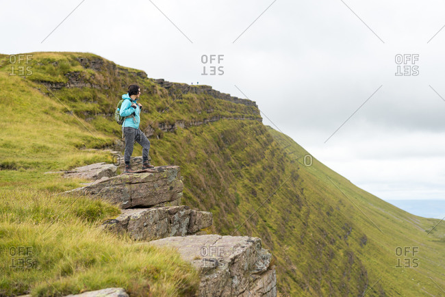 A woman looks out from a high escarpment while hiking in the Brecon Beacons National Park mountain range