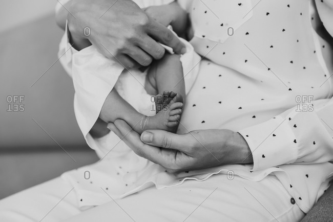 Parent holding newborn baby with focus on baby's foot in black and white