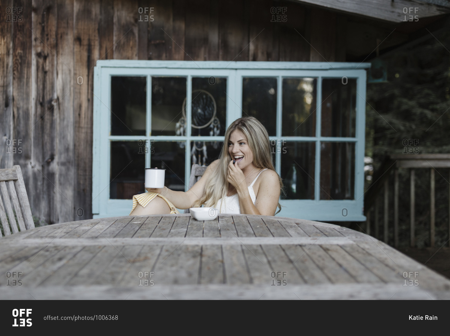 Happy blonde woman having coffee on deck of a cabin in the woods