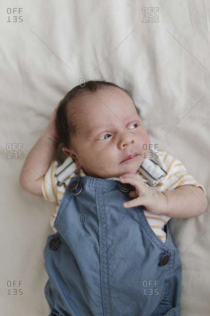 Baby boy wearing overalls lying on white blanket