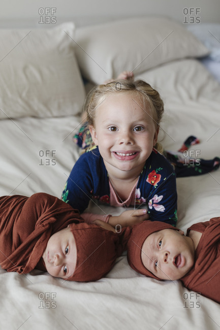 Big sister lying with twin baby brothers on bed