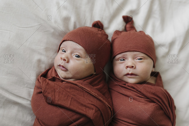 Identical twin baby boys in matching outfits on bed together