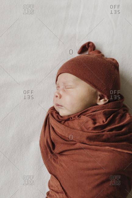 Baby boy lying on bed swaddled in a brown blanket and matching cap