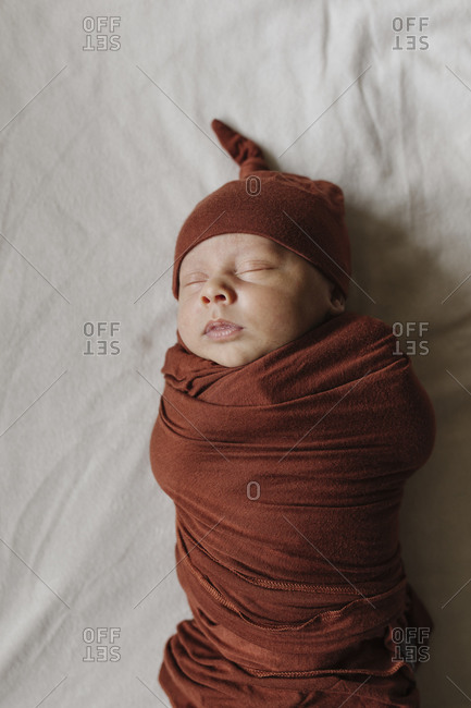 Baby boy sleeping on bed swaddled in a brown blanket and matching cap