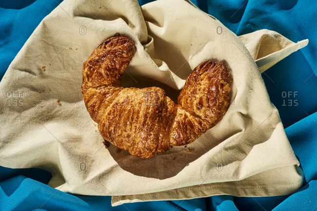 Appetizing croissant in a beige napkin, on a wrinkled blue fabric