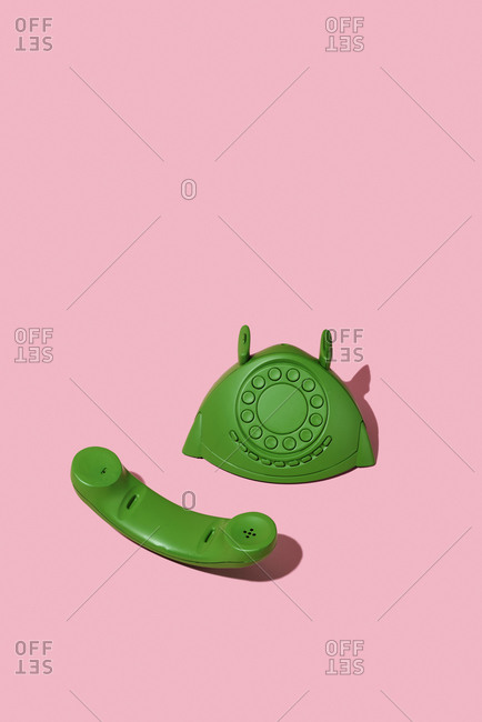 Green telephone, off the hook, on a pink background