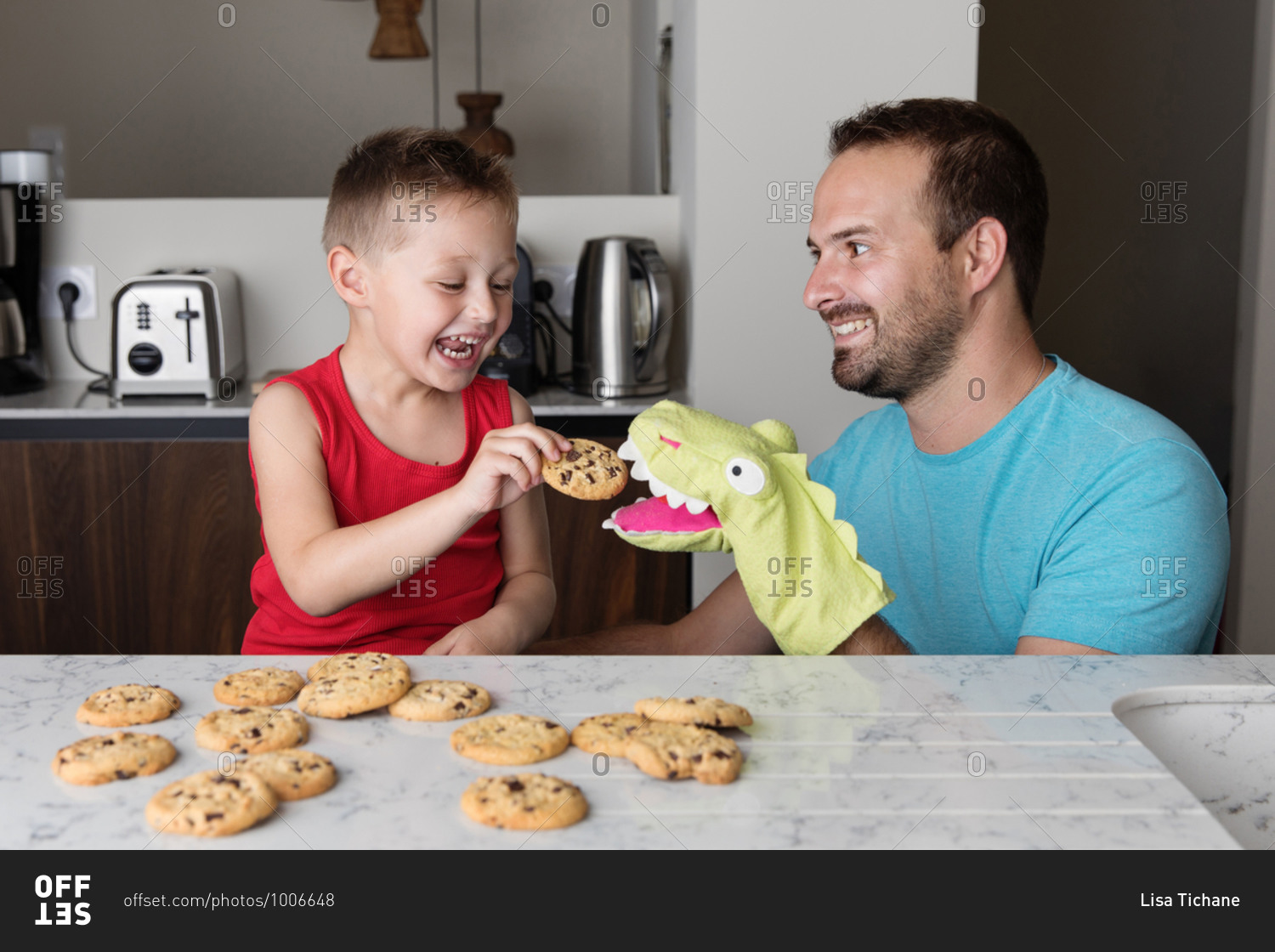 Happy father and son feeding glove puppet in kitchen while eating cookies