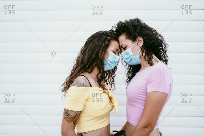 Lesbian couple wearing masks with face to face standing against wall in city