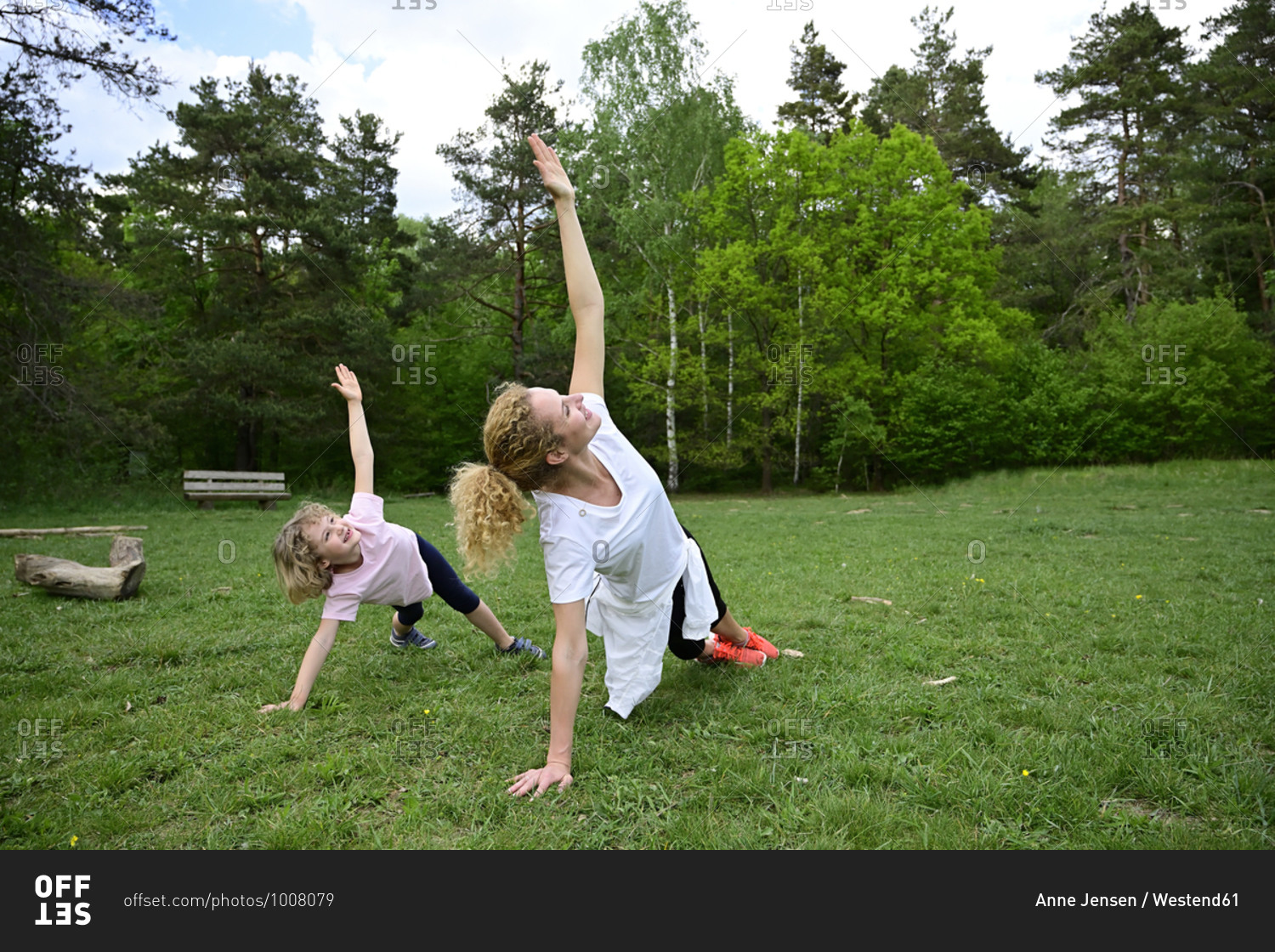 Mother and daughter practicing side plank pose on grassy land in forest