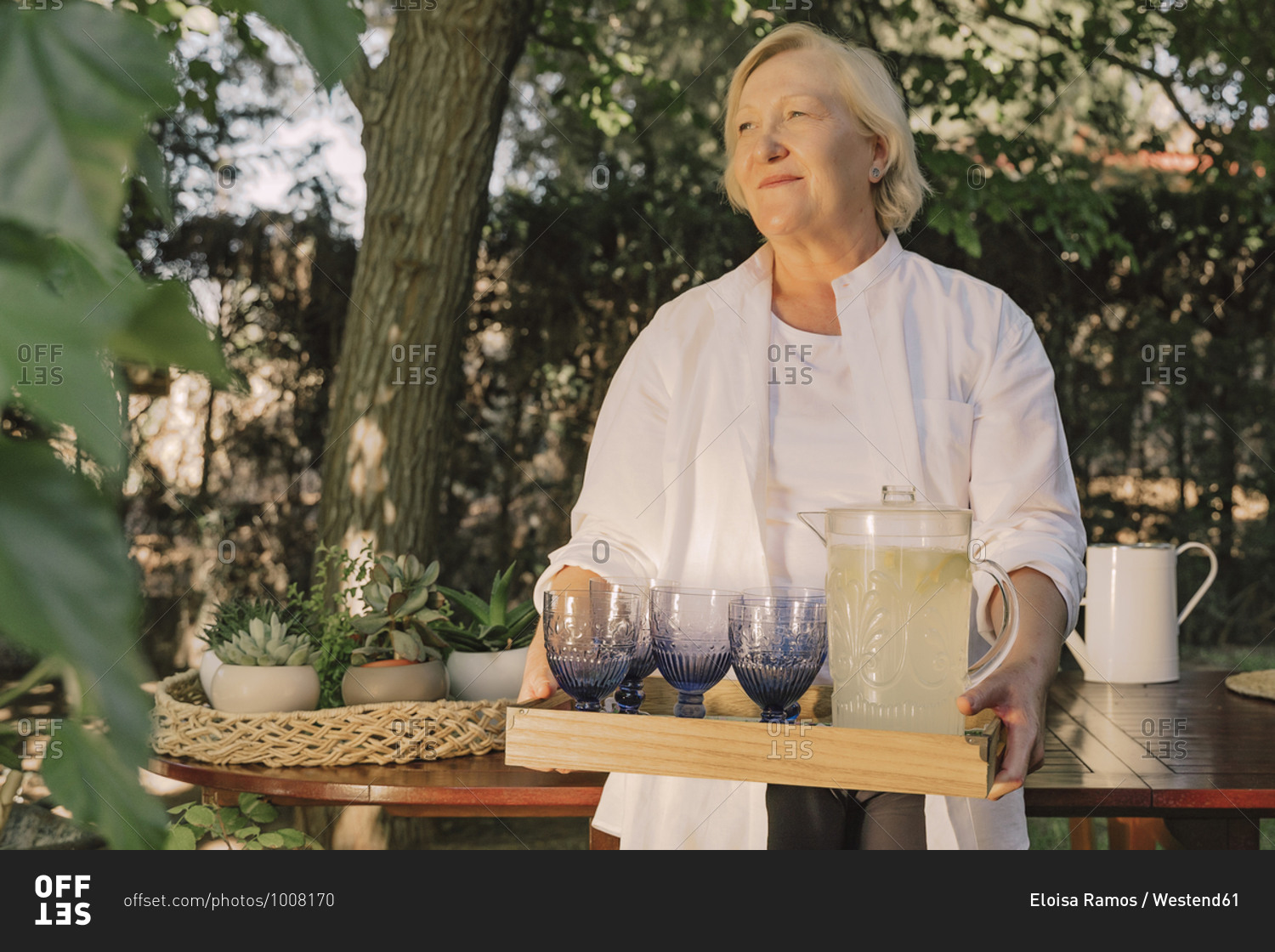 Thoughtful senior woman carrying tray with drinks while standing in yard