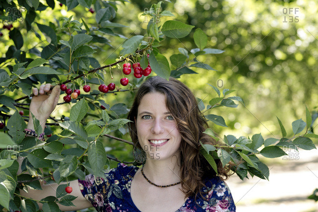 Close-up of smiling young woman holding cherry plant in farm