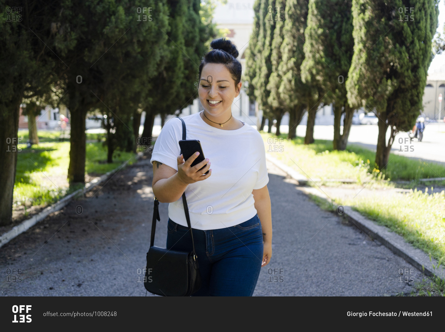 Smiling curvy young woman using mobile phone in a public park