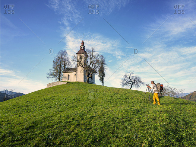 Slovenia- Upper Carniola- Municipality of Skofja Loka- Man photographing Saint Thomass Church in autumn