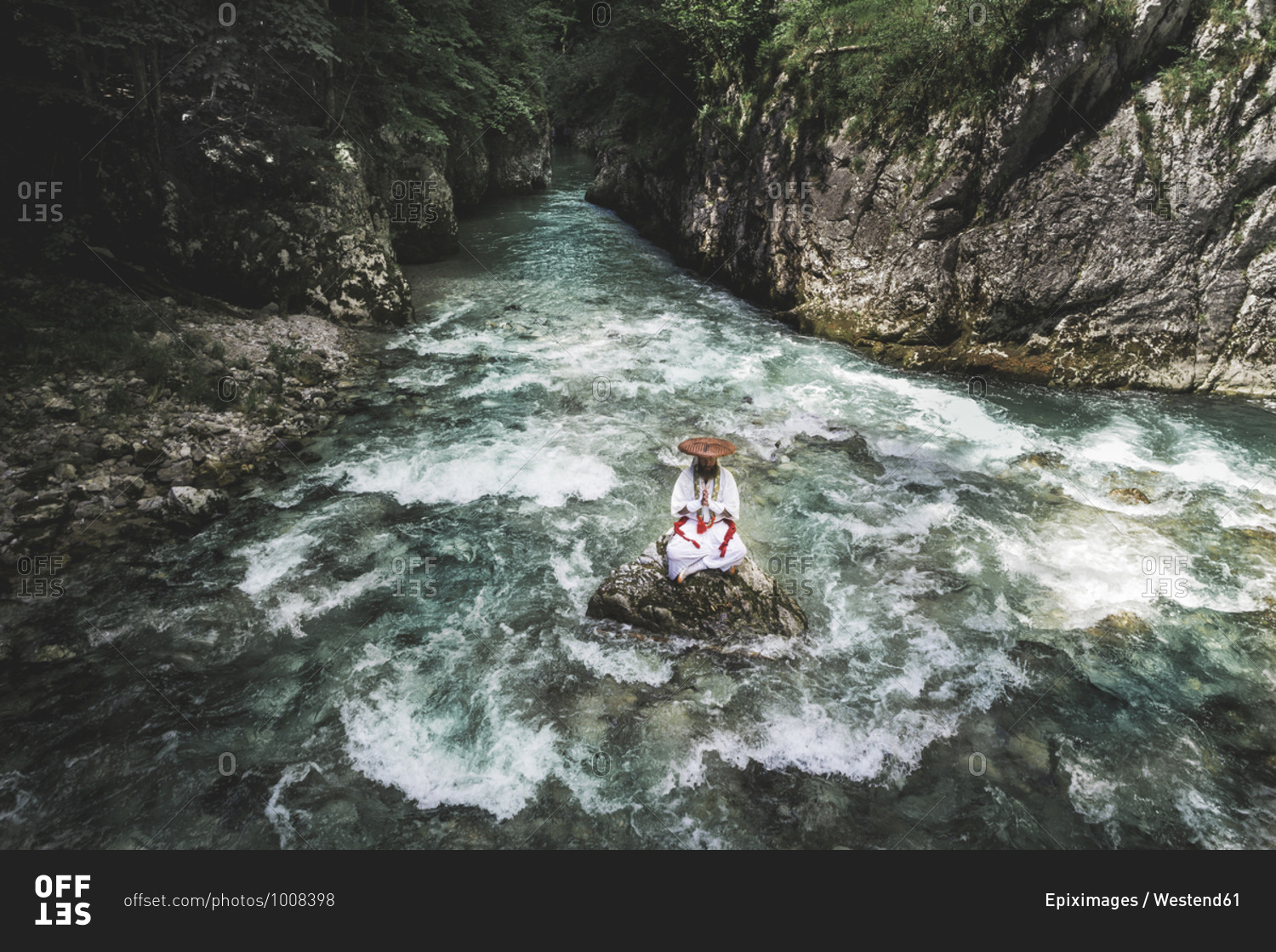 European yamabushi monk sitting on rock in the middle of river and meditating