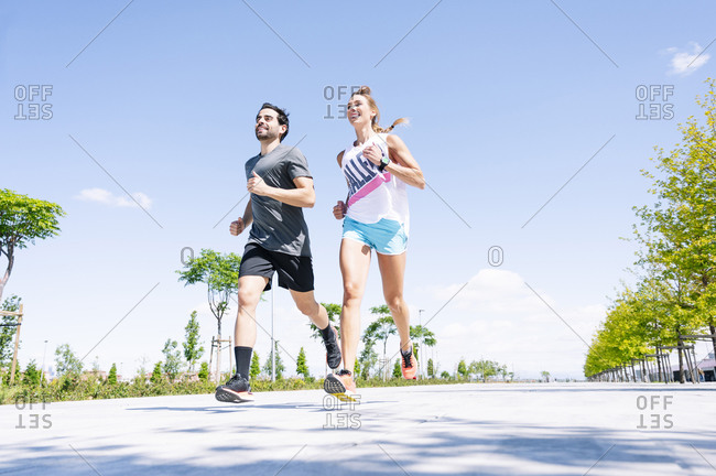 Mid adult couple running on road against blue sky during sunny day