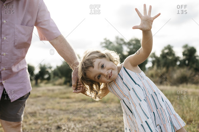 Cheerful cute girl holding grandfather's hand while standing on land against sky