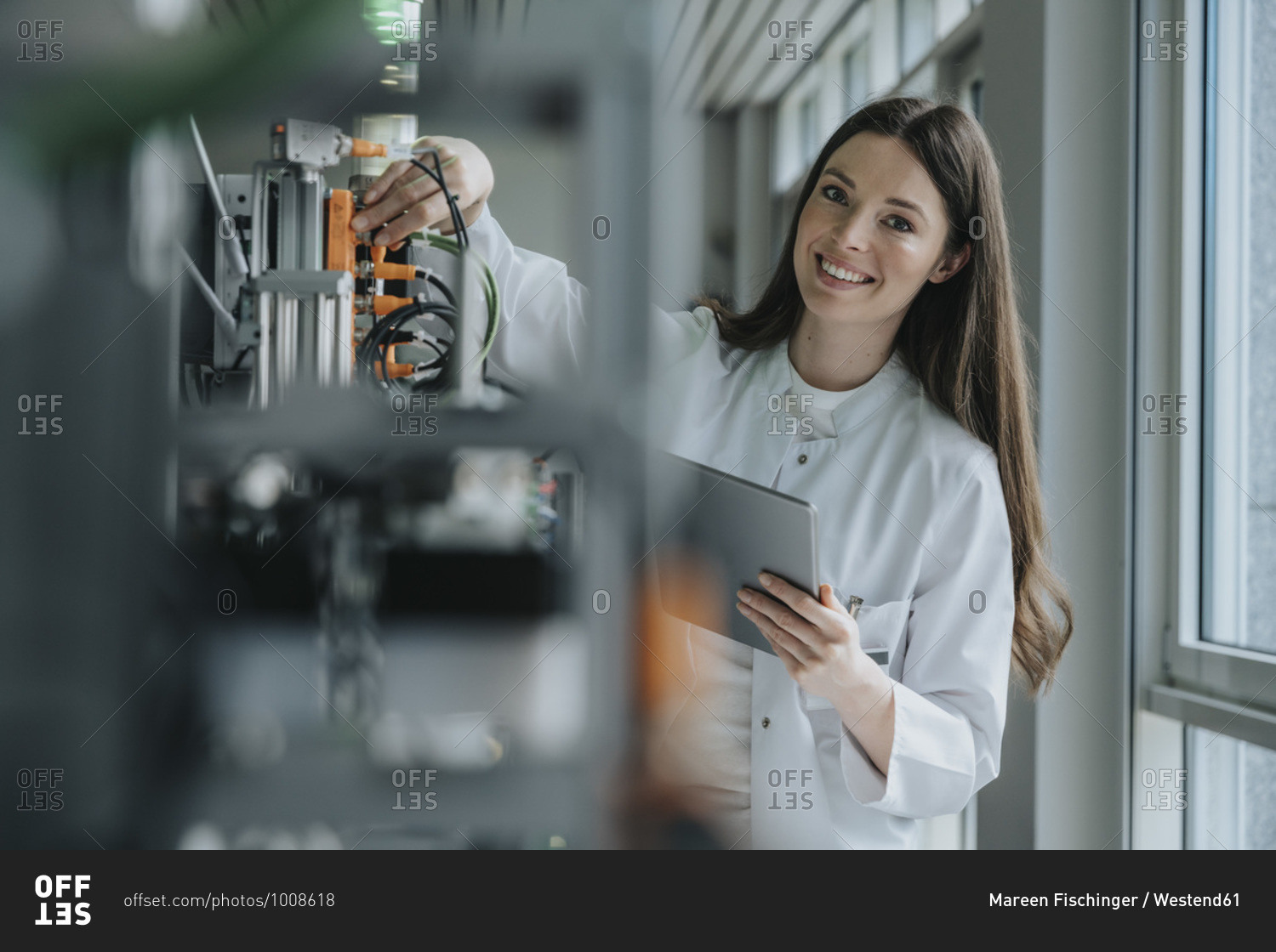 Smiling female scientist holding digital tablet inventing machinery in factory