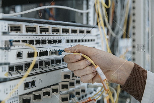 Close-up of woman plugging fiber optic cable in equipment at data center