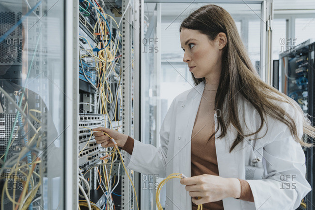 Young woman plugging transceiver on fiber optic cable in data center