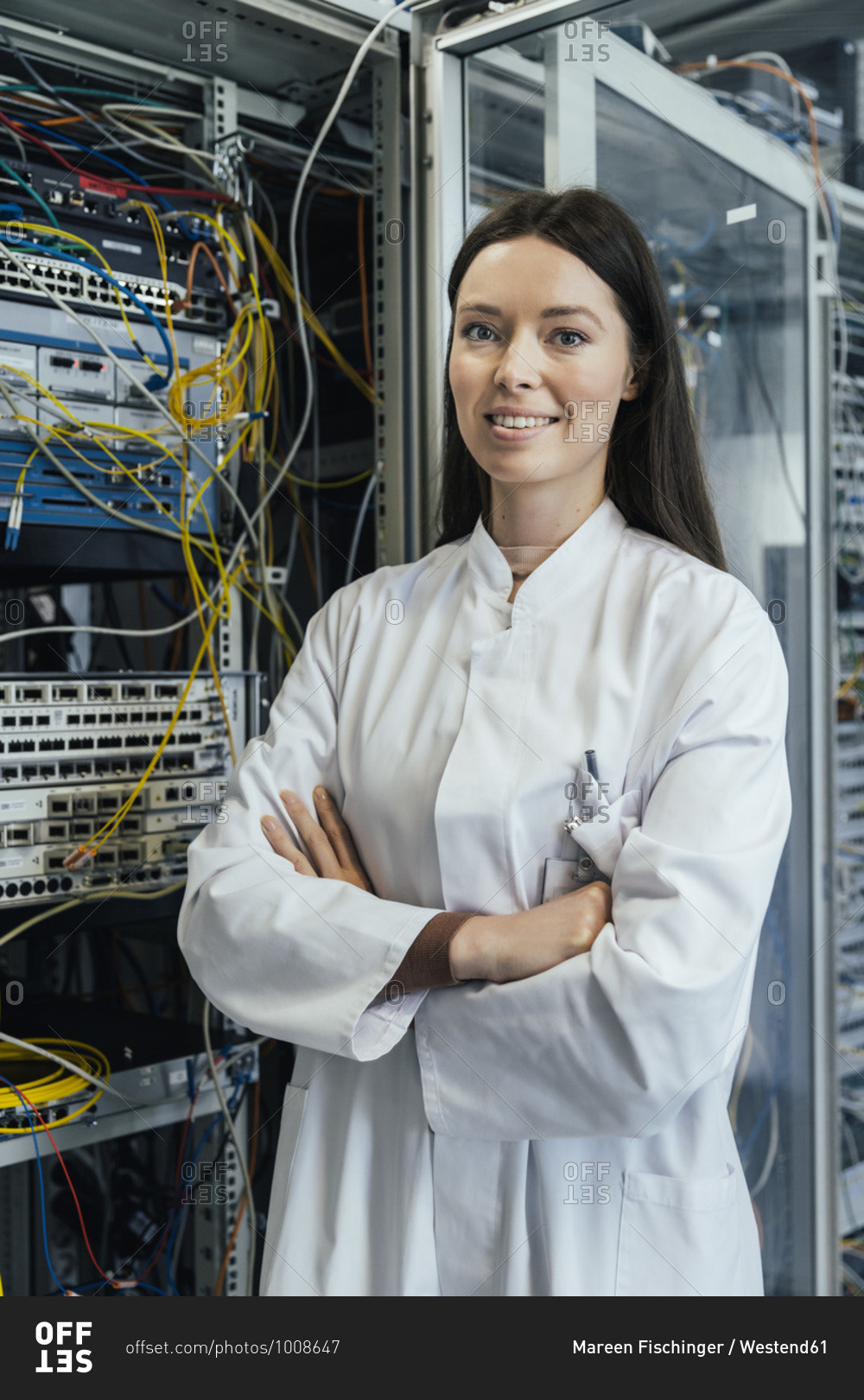 Female IT professional with arms crossed standing in server
room stock photo - OFFSET