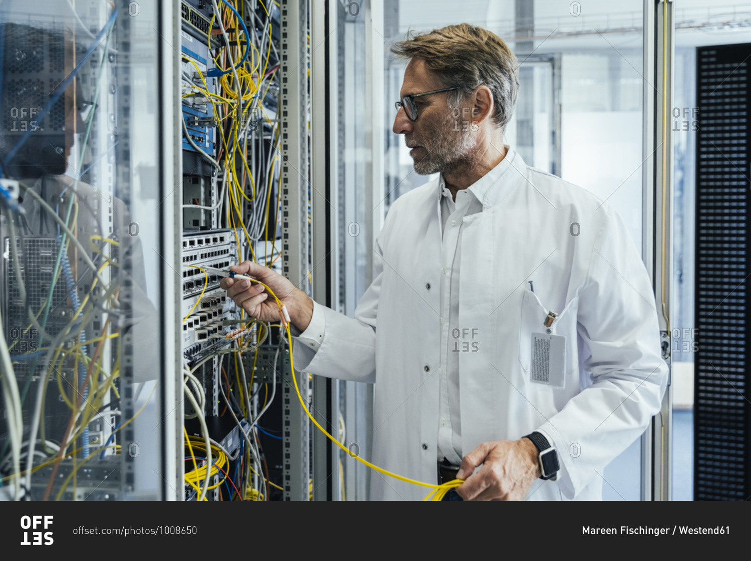 Mature man plugging transceiver on fiber optic cable into rack