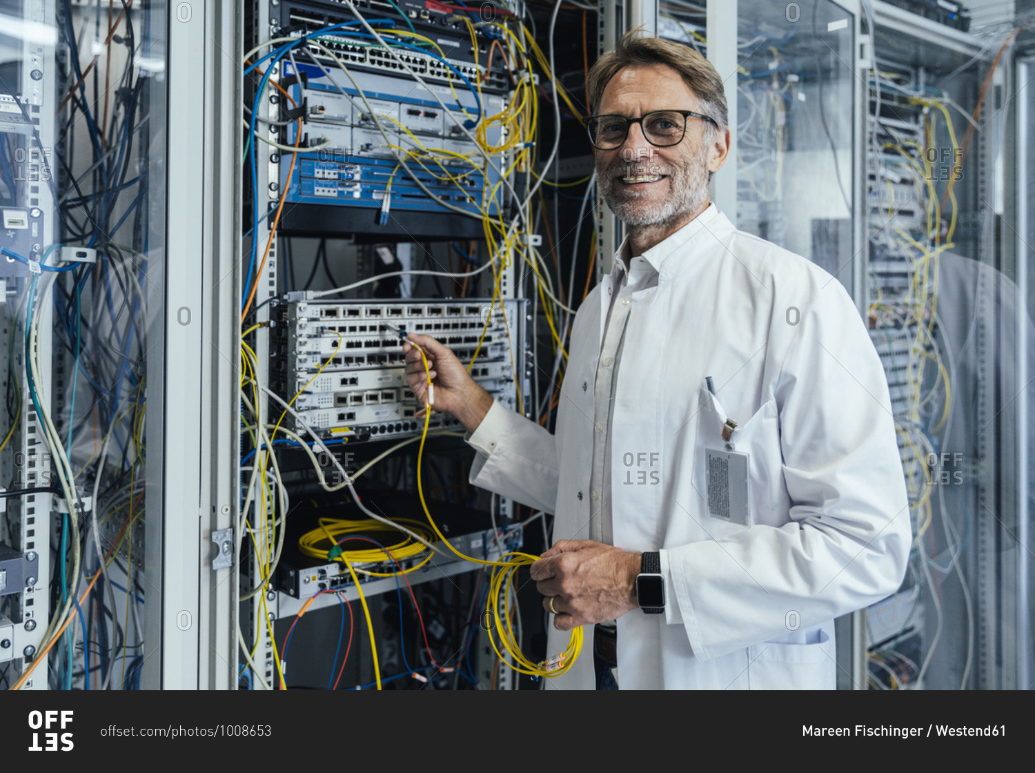 Smiling mature man plugging transceiver on fiber optic cable in data center