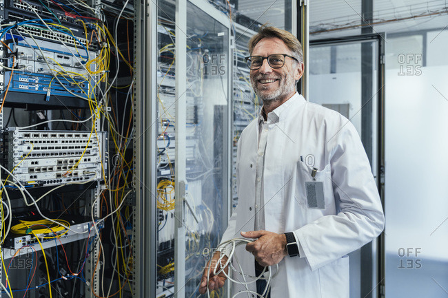 Male IT professional holding cables standing by network server in date center