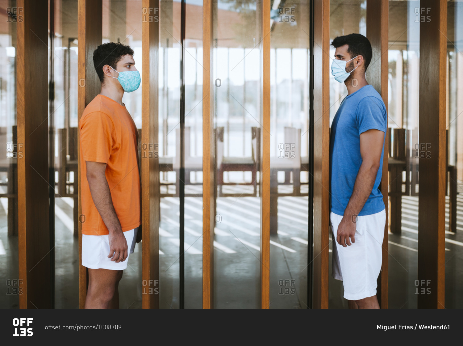 Male friends wearing masks looking at each other while standing by built structure