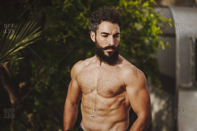 Attractive shirtless man standing in front of shrubs