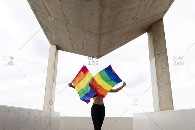 Mid adult woman waving rainbow flags while standing on built structure against sky