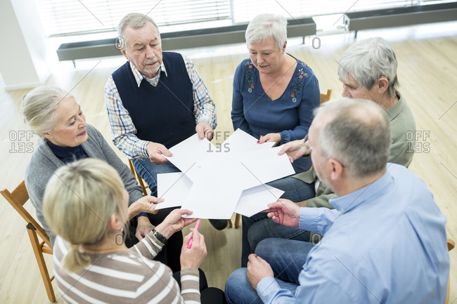 Group of seniors attending therapy group in retirement home- using sheets of paper