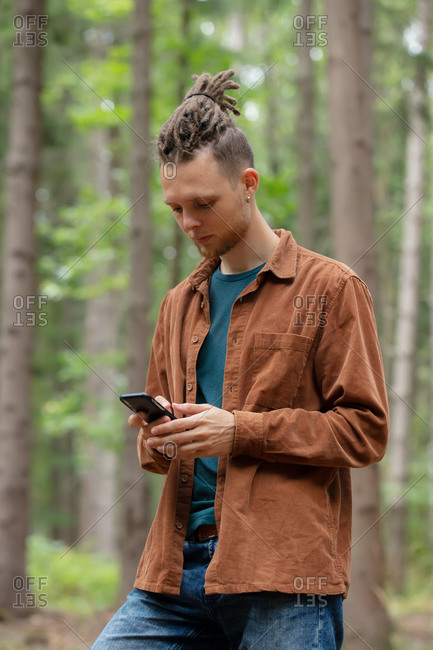Young man with a mobile phone is looking for direction in the forest
