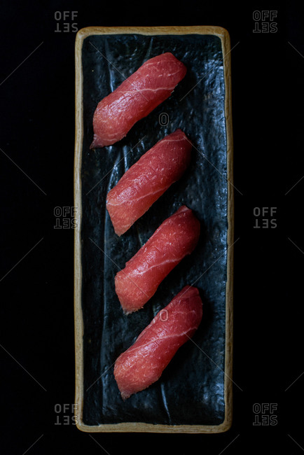 From above of delicious salmon sushi served on plate with chopstick in restaurant on black background