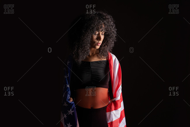 Black woman with curly hair wrapped on the USA flag representing black lives matter activism movement looking away