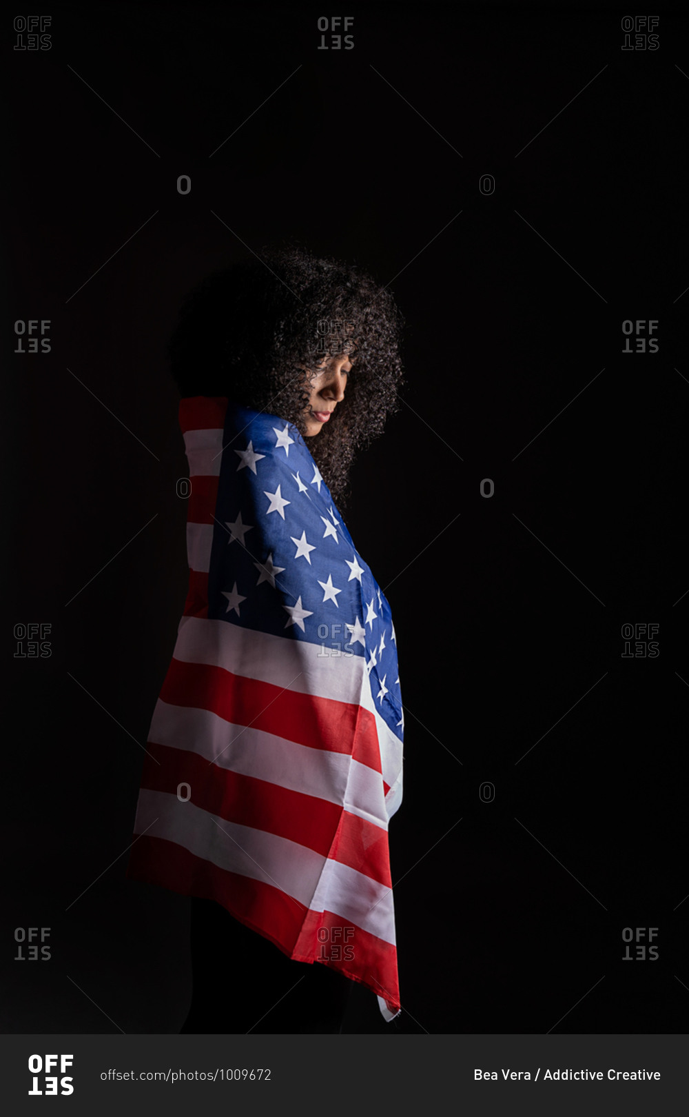Side view of a black woman with curly hair wrapped on the USA flag representing black lives matter activism movement looking down