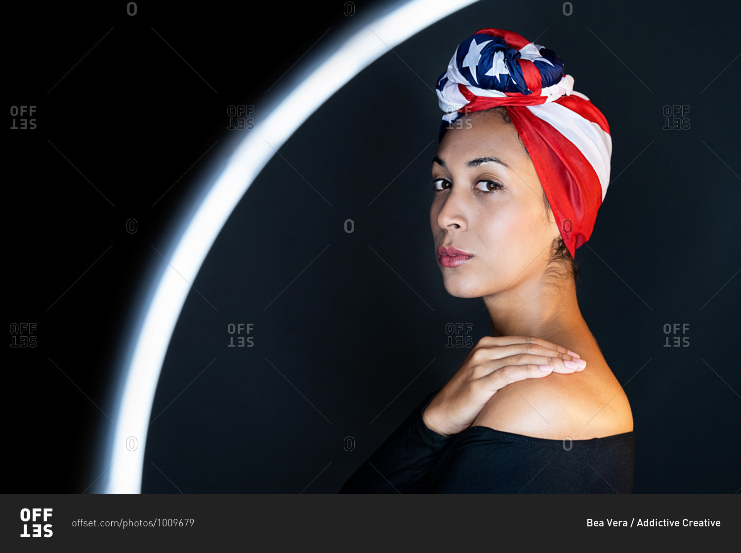 Side view of thoughtful black female standing in front of a led ring light wearing proudly the United States of America colors as a head wrap looking at camera