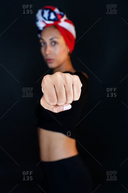 Portrait of a thoughtful black female wearing proudly the United States of America colors as a head wrap and showing fist towards the camera on black background