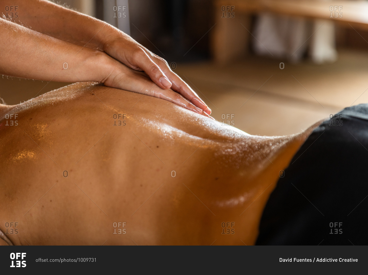 Side view of crop anonymous master performing ayurvedic massage with aromatic oil on back of relaxed customer in modern salon
