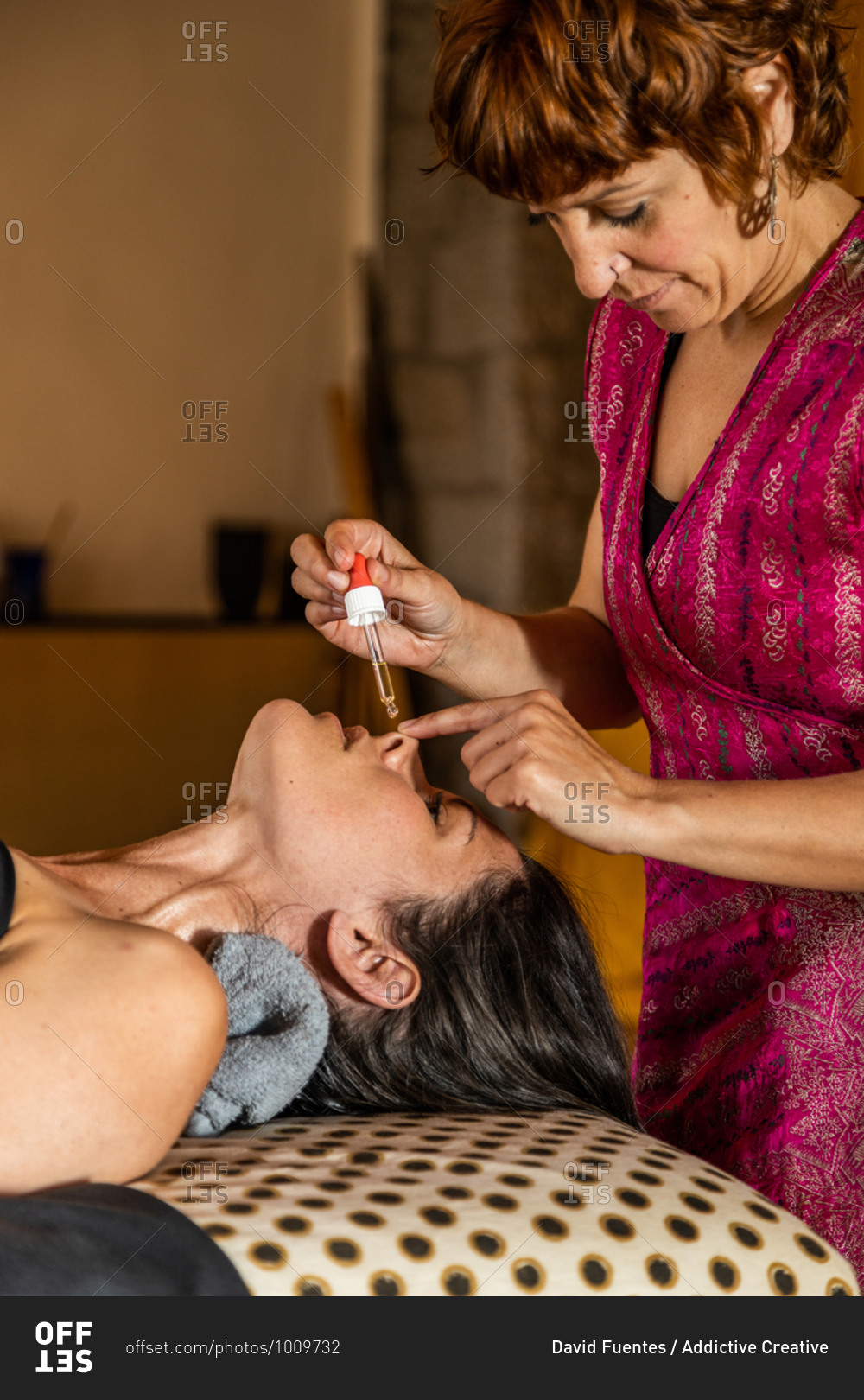 Side view of female master with dropper applying essential oil into nose of client during ayurvedic healing procedure