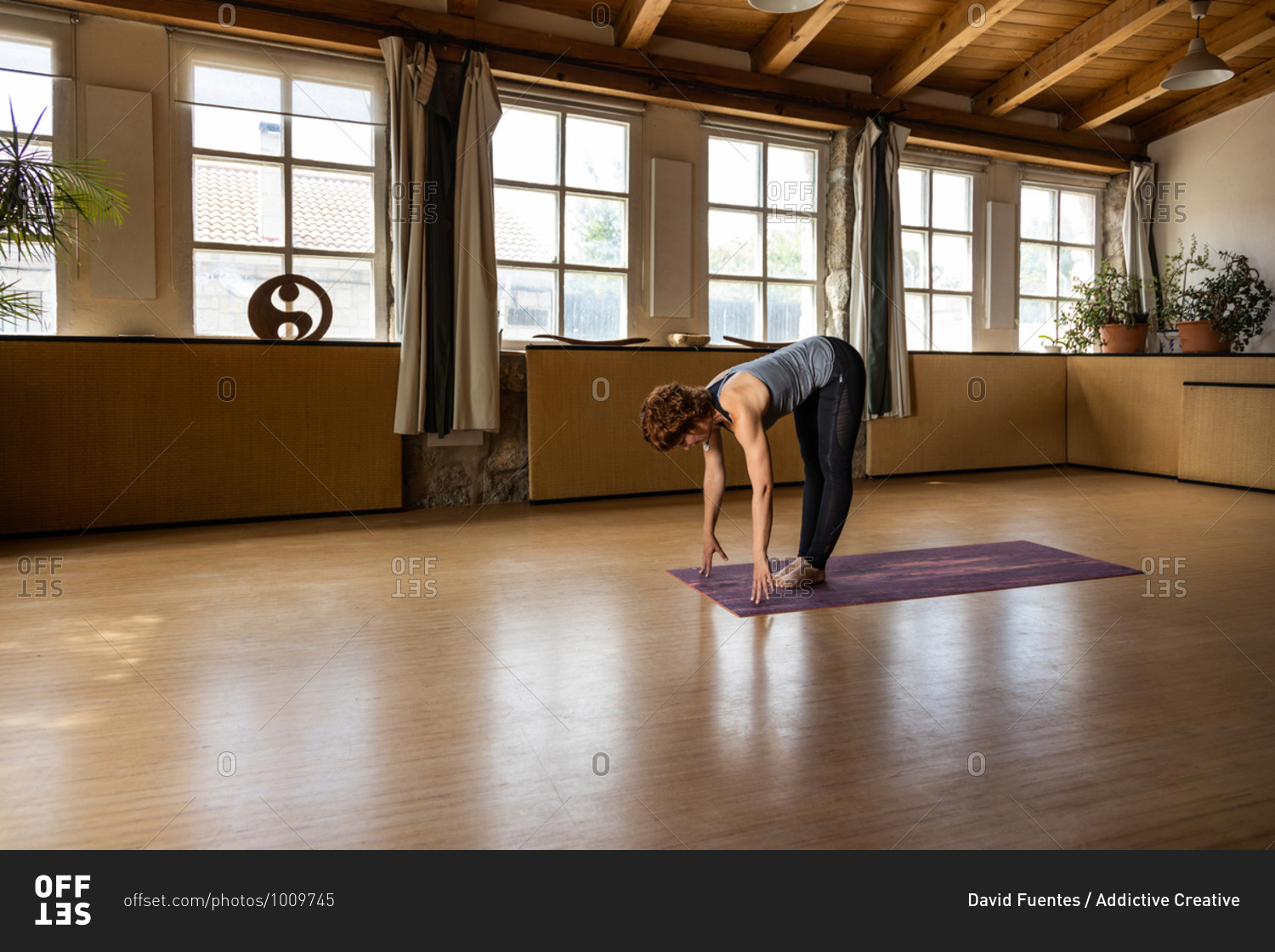 Full body side view of focused female in sportswear standing in Ardha Uttanasana pose during Shakti yoga practice in spacious room with wooden interior